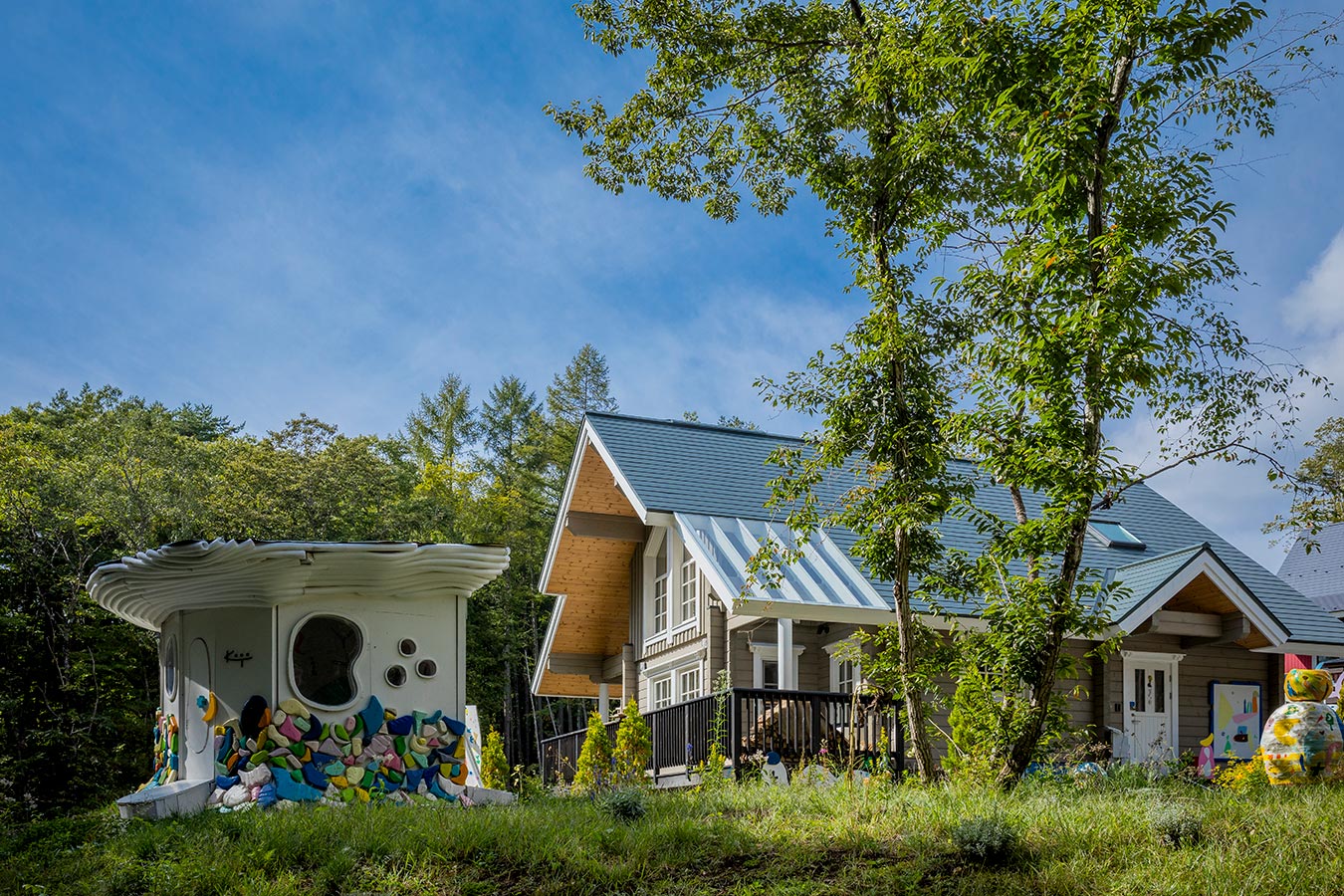 大屋根デザインのログハウスに色鮮やかな離れやオブジェが童話の世界のような光景。